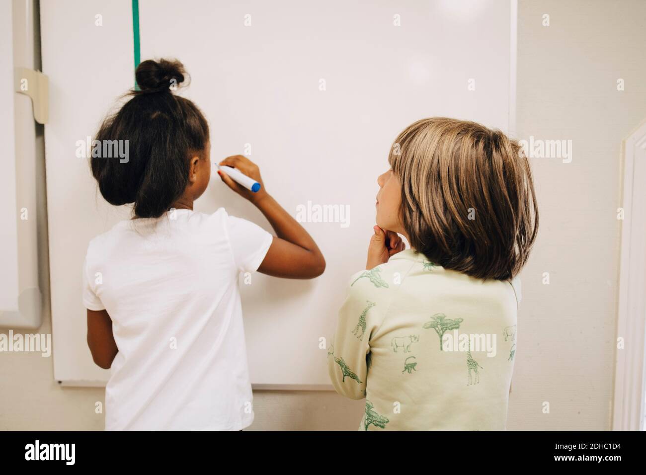 Boy looking at schoolgirl writing on whiteboard in elementary school Stock Photo