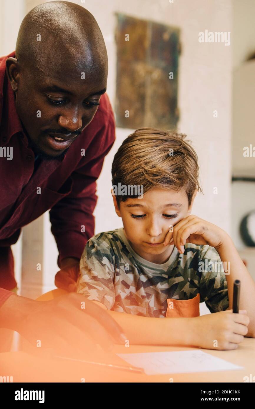Male teacher assisting boys at desk in classroom Stock Photo - Alamy