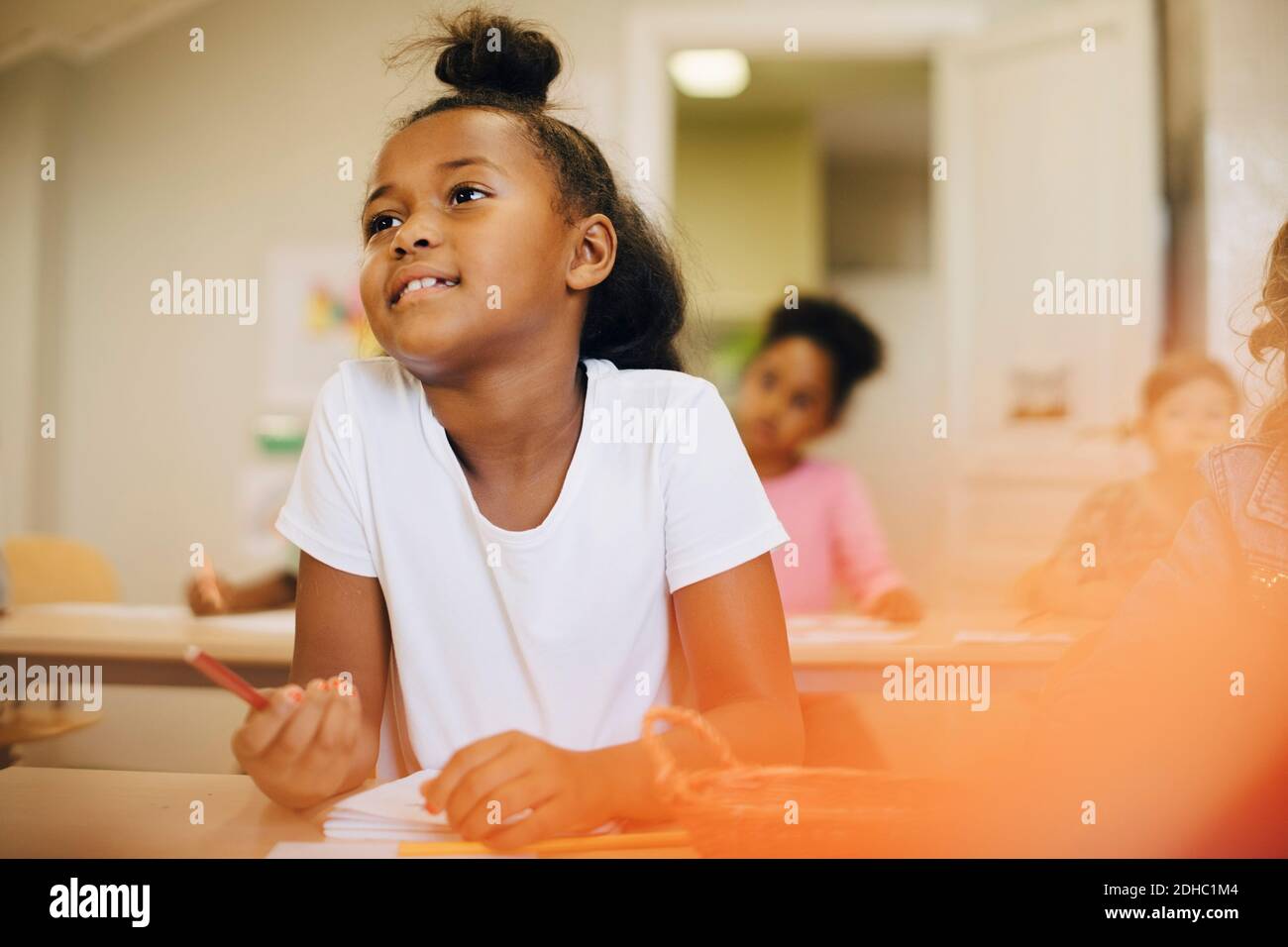 Schoolgirl looking away while sitting at desk in classroom Stock Photo