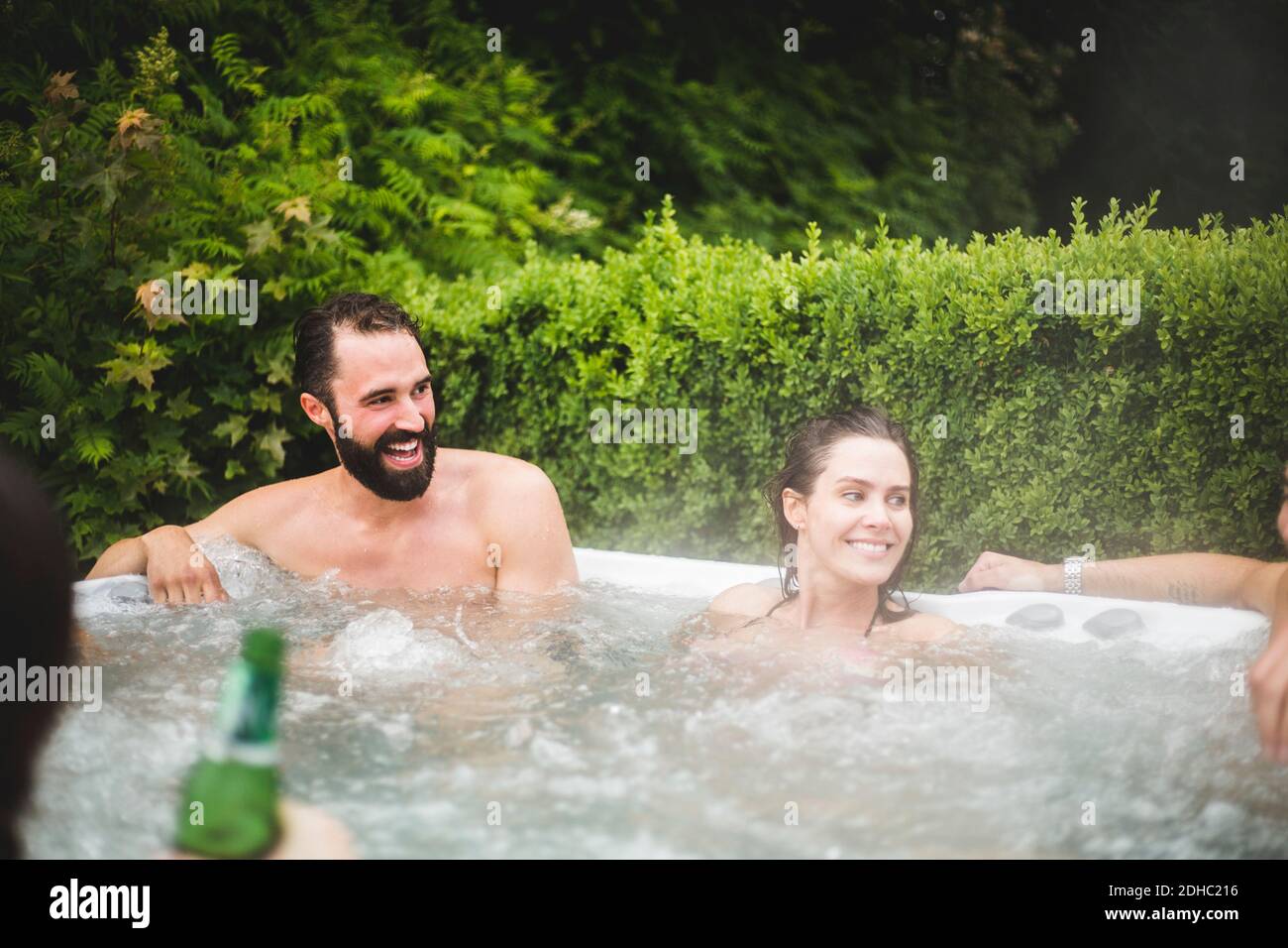 Cheerful male and female friends looking away while enjoying in hot tub Stock Photo