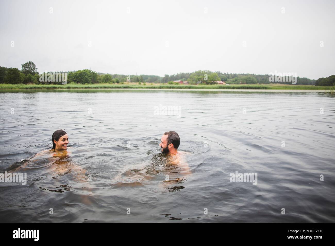 Happy male and female friends swimming in lake against clear sky during weekend Stock Photo