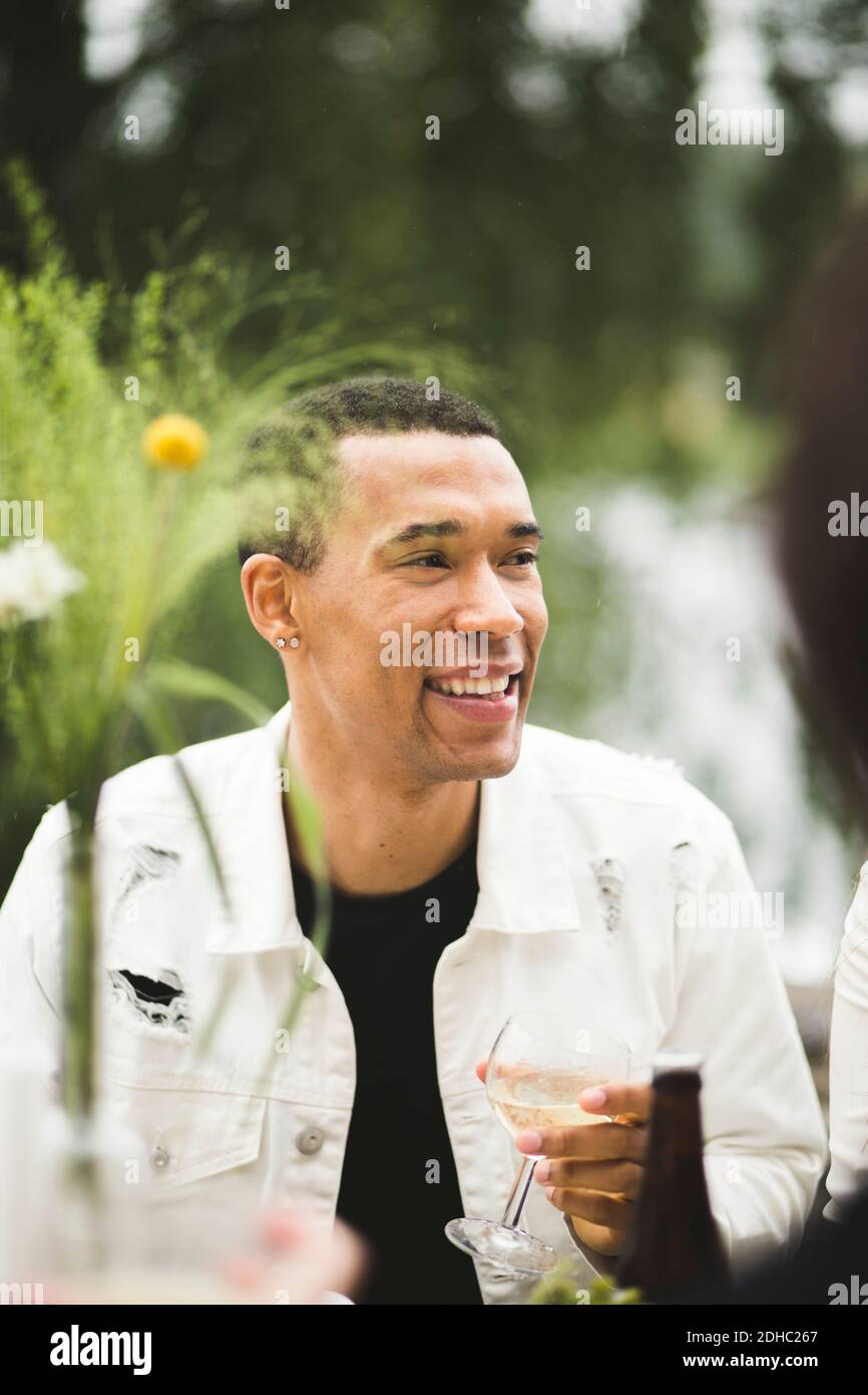 Smiling young man looking away while holding wineglass during dinner party Stock Photo