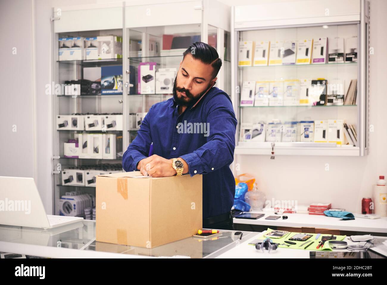 Male owner talking on mobile phone while packing box at counter in electronics store Stock Photo