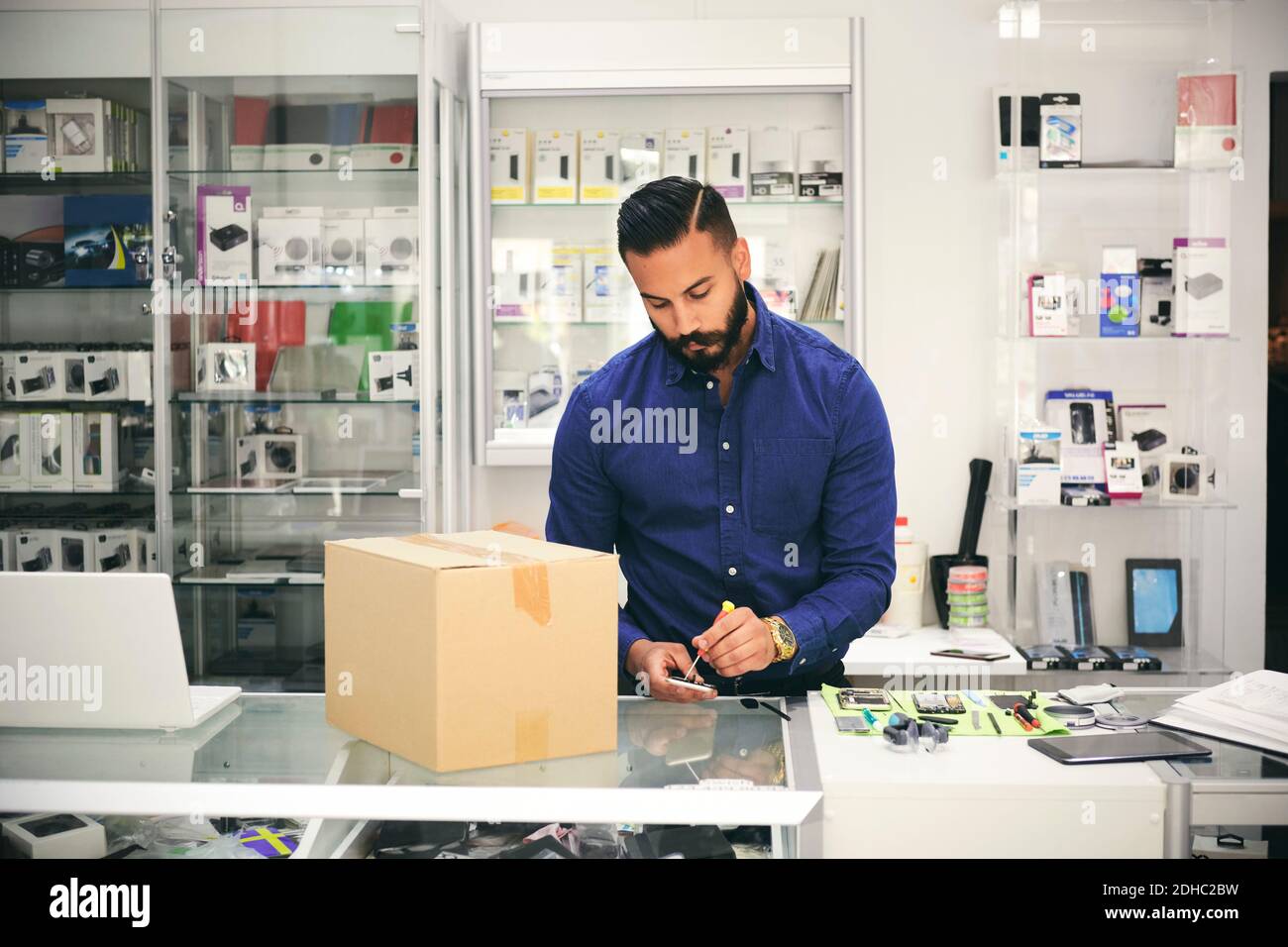 Technician repairing mobile phone at counter in electronics store Stock Photo