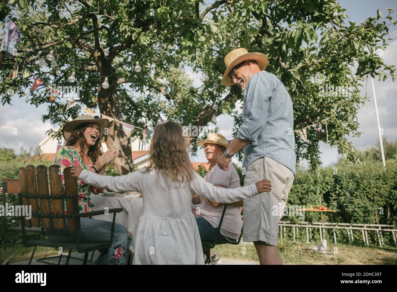 Family applauding while looking at senior man and girl dancing during garden party Stock Photo