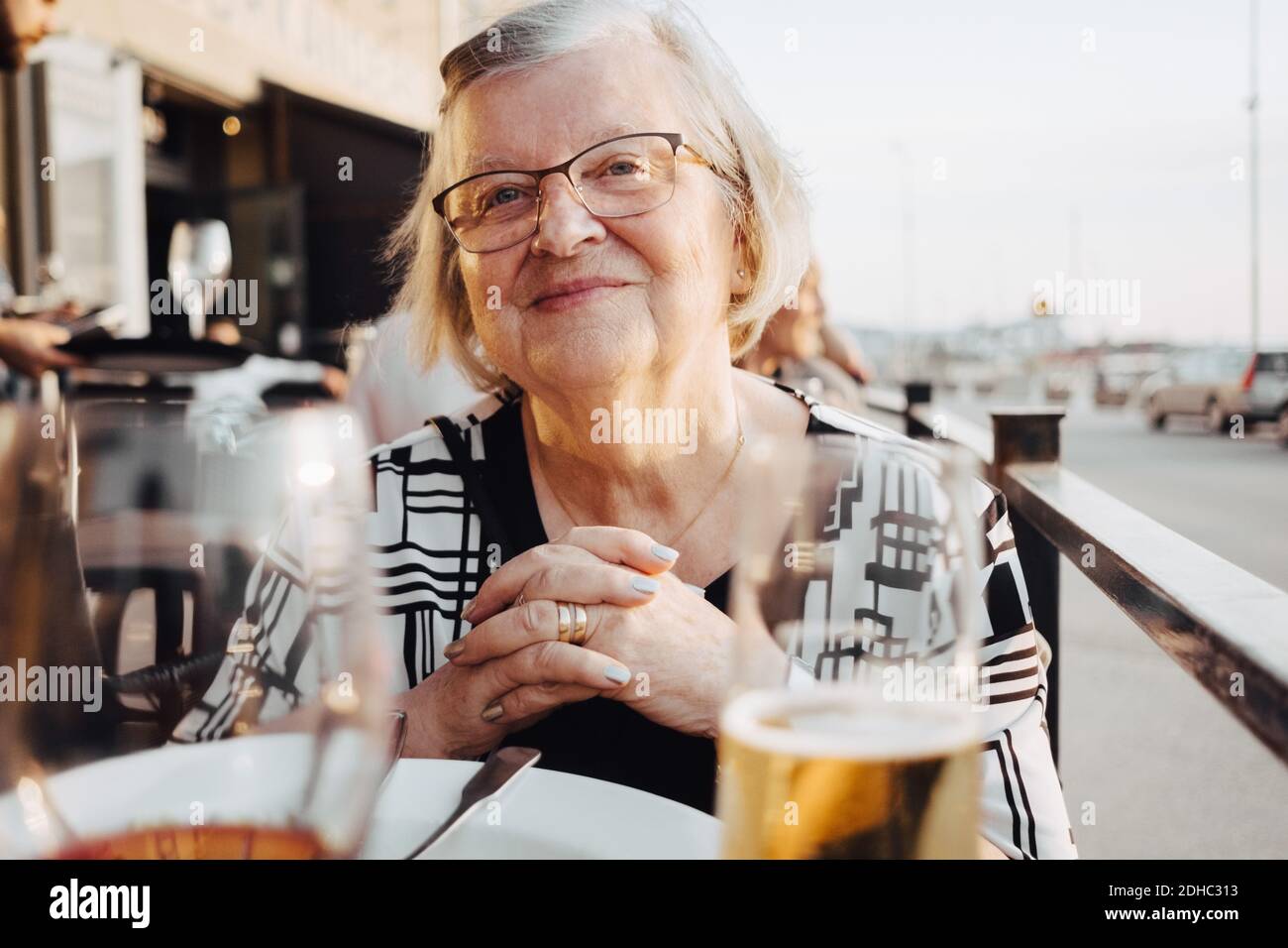 Smiling senior female tourist sitting with hands clasped at restaurant Stock Photo