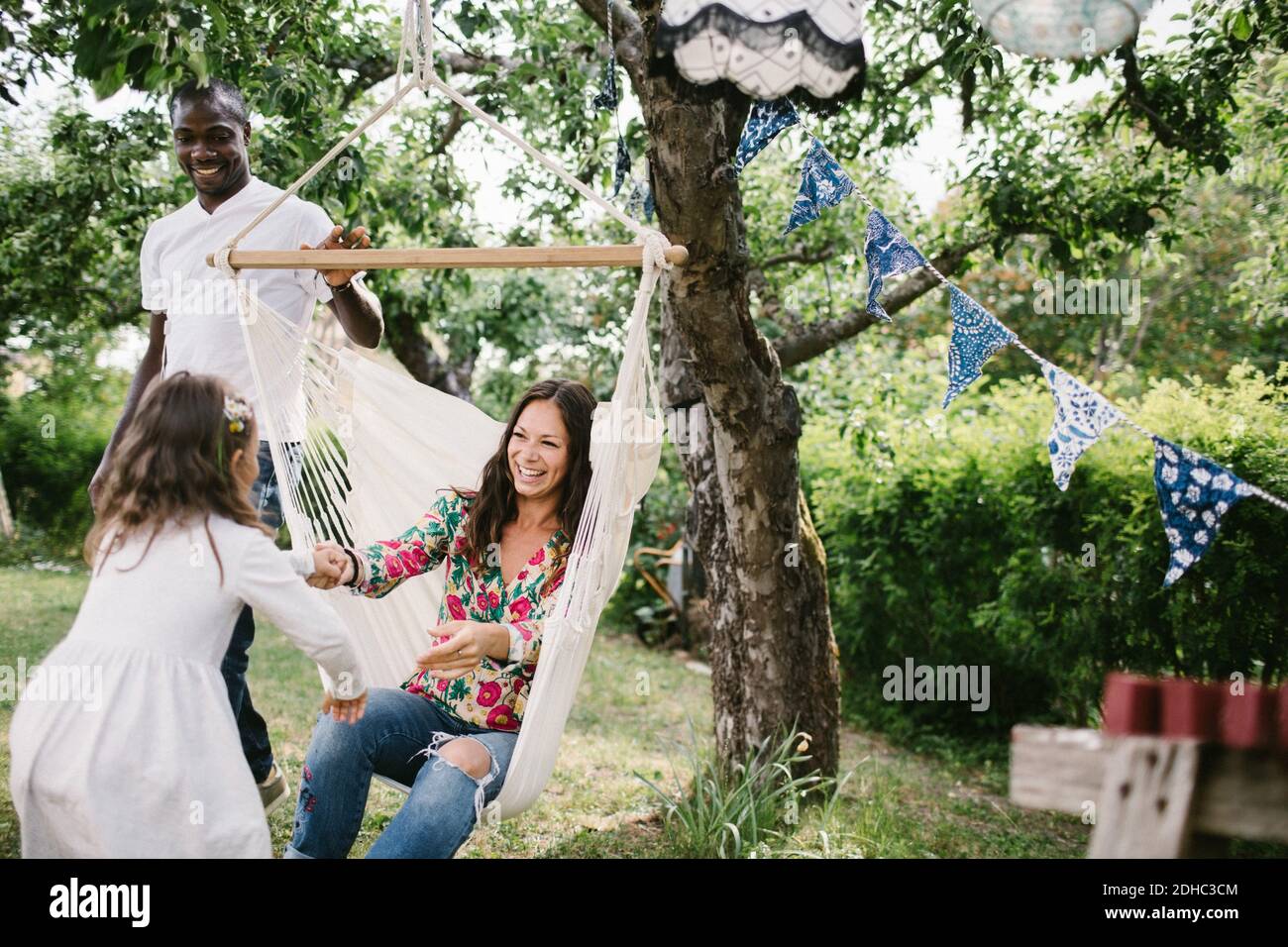 Father pushing hammock while happy woman holding hand of daughter in backyard Stock Photo