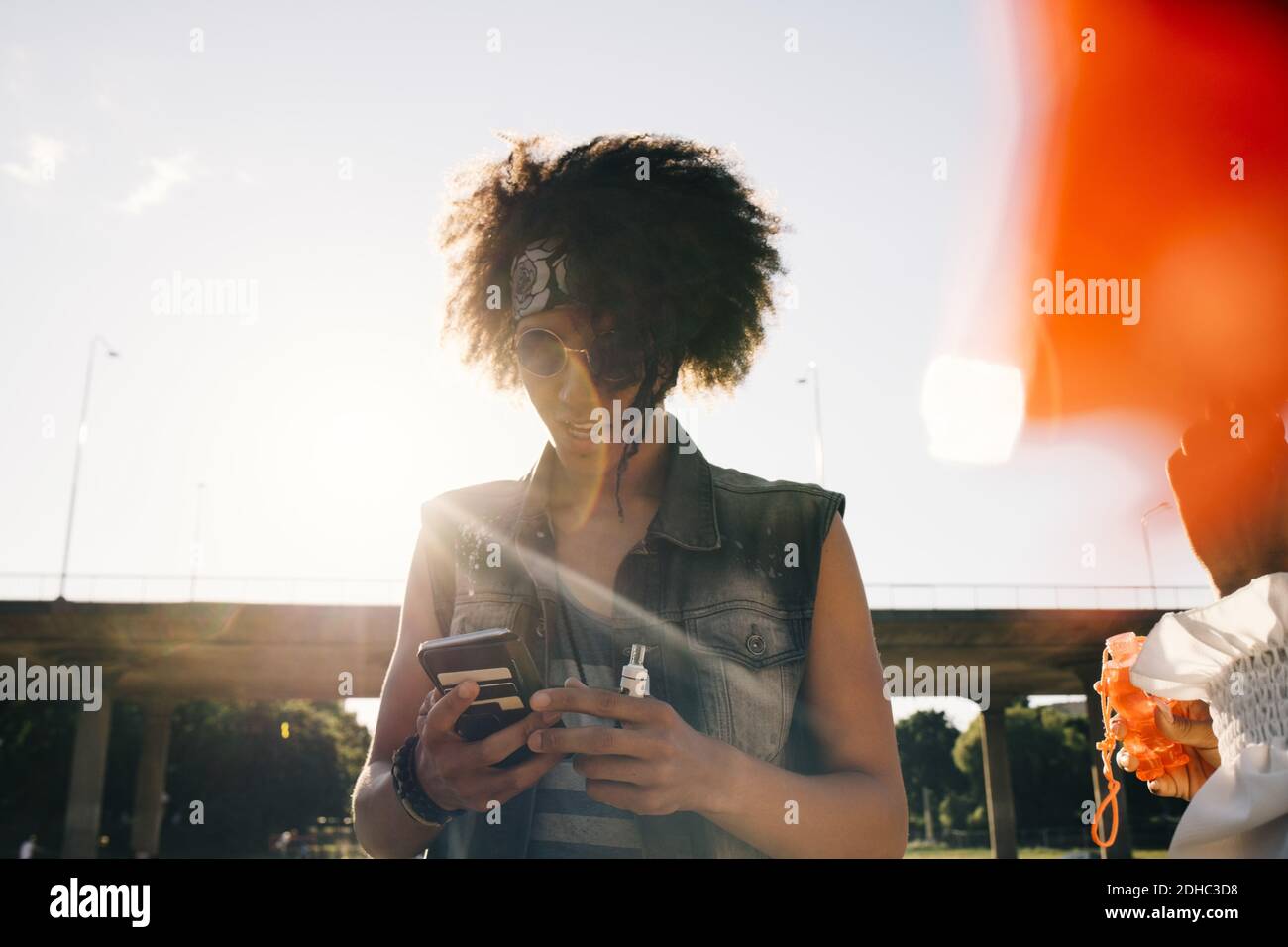 Young man with electronic cigarette using mobile phone in summer Stock Photo