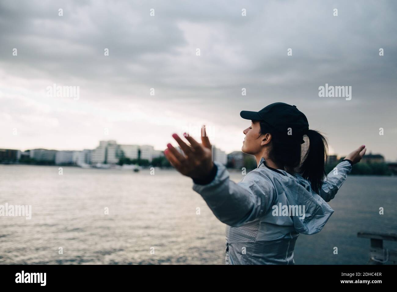 Female athlete standing with arms outstretched by sea against sky in city Stock Photo