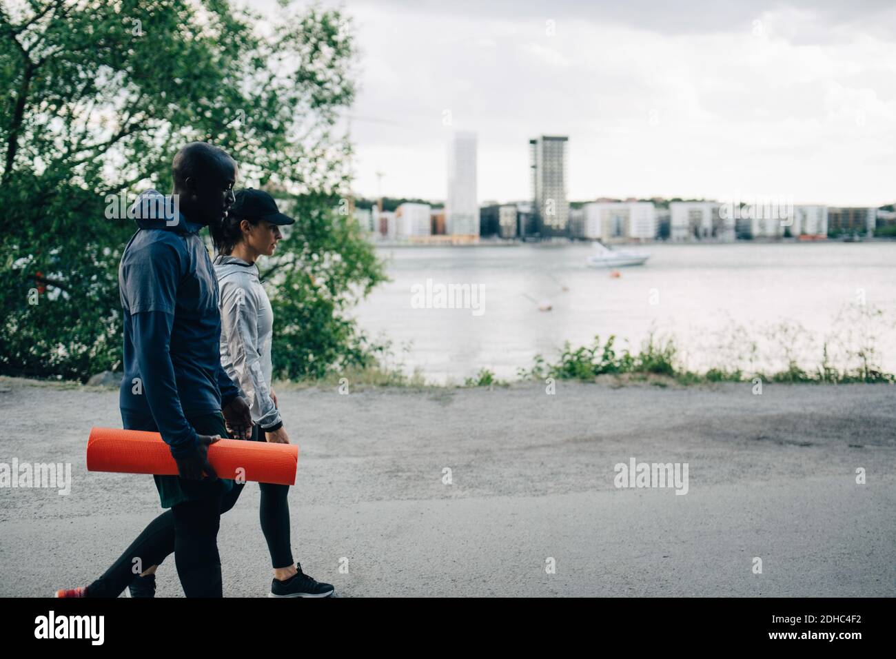 Male athlete holding yoga mat while walking with female friend on road in city Stock Photo