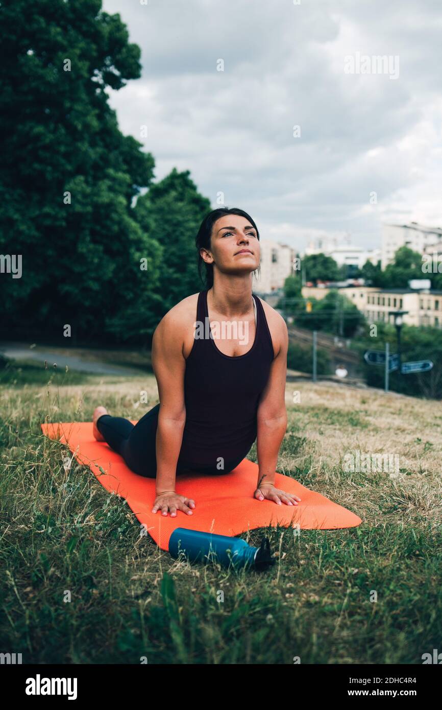 Young woman practicing cobra pose on field in city Stock Photo