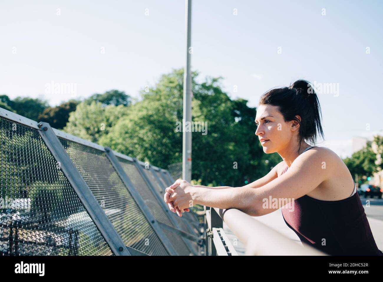 Side view of exhausted sportswoman leaning on railing at bridge Stock Photo