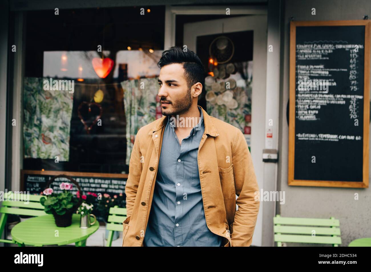 Thoughtful young man looking away while standing against restaurant Stock Photo