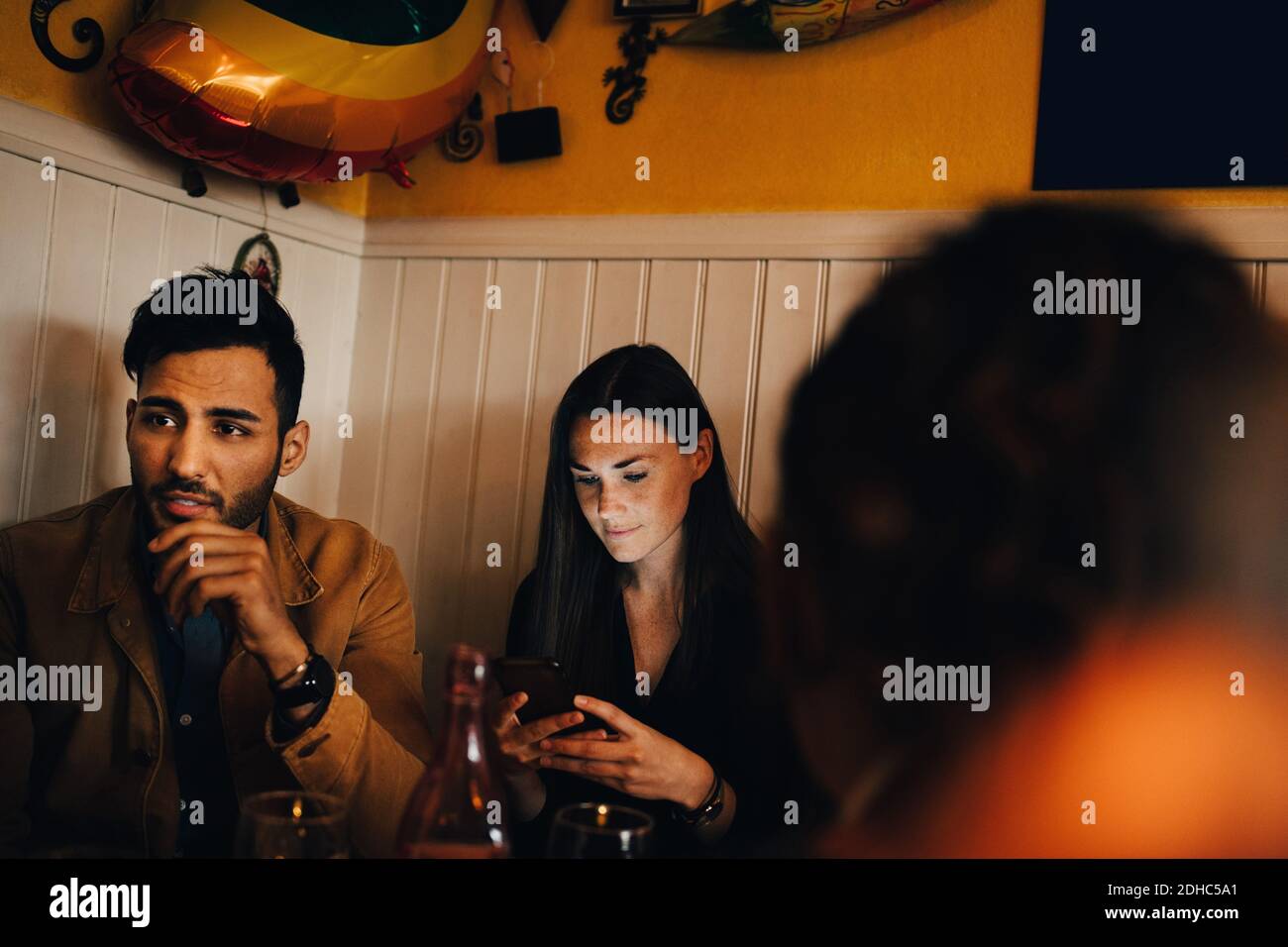 Young woman using smart phone while sitting by man in restaurant Stock Photo
