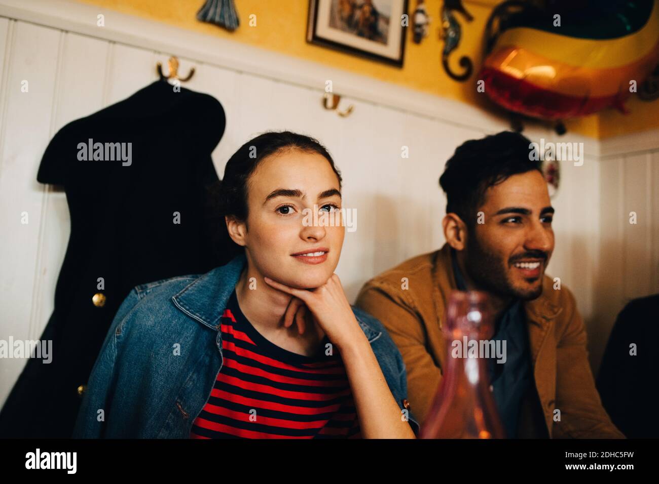 Portrait of smiling young woman sitting with hand on chin by man at restaurant during lunch party Stock Photo