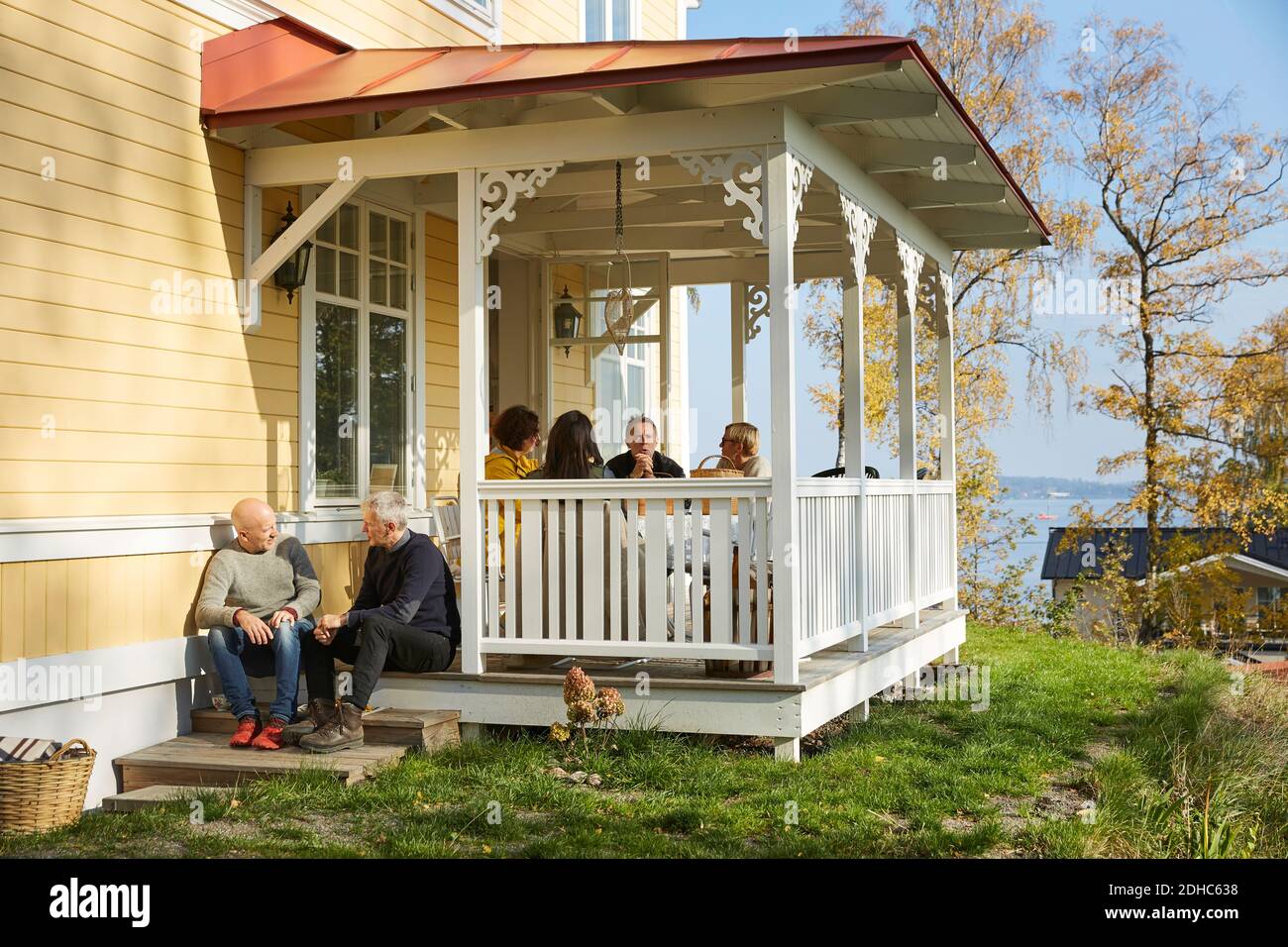 Friends talking while sitting on porch outside mansion Stock Photo