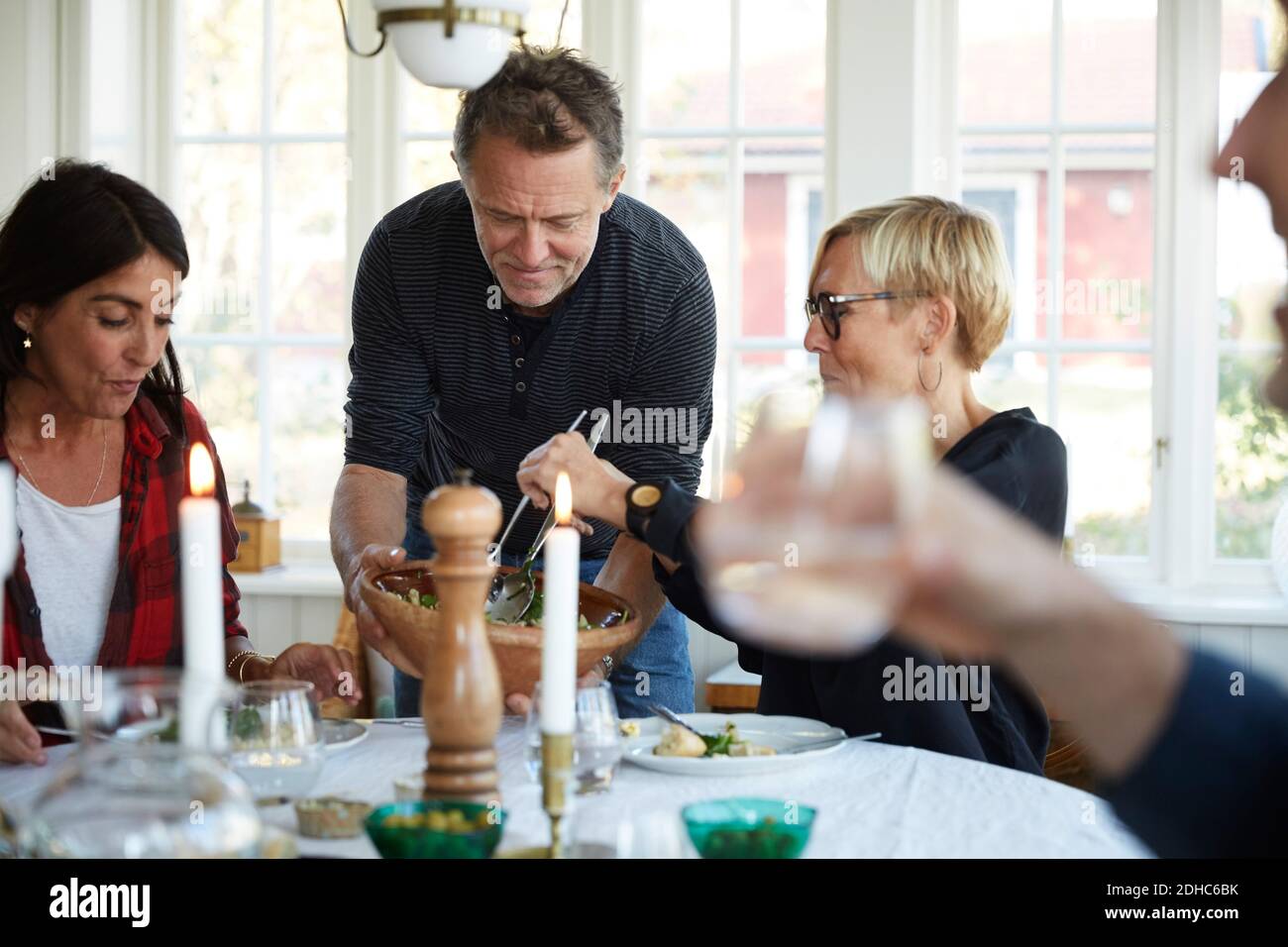 Mature man serving food to female friends at home Stock Photo