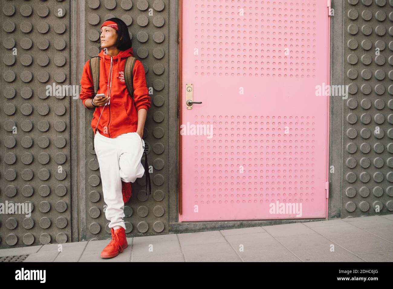 Thoughtful young man looking away while holding mobile phone against wall Stock Photo