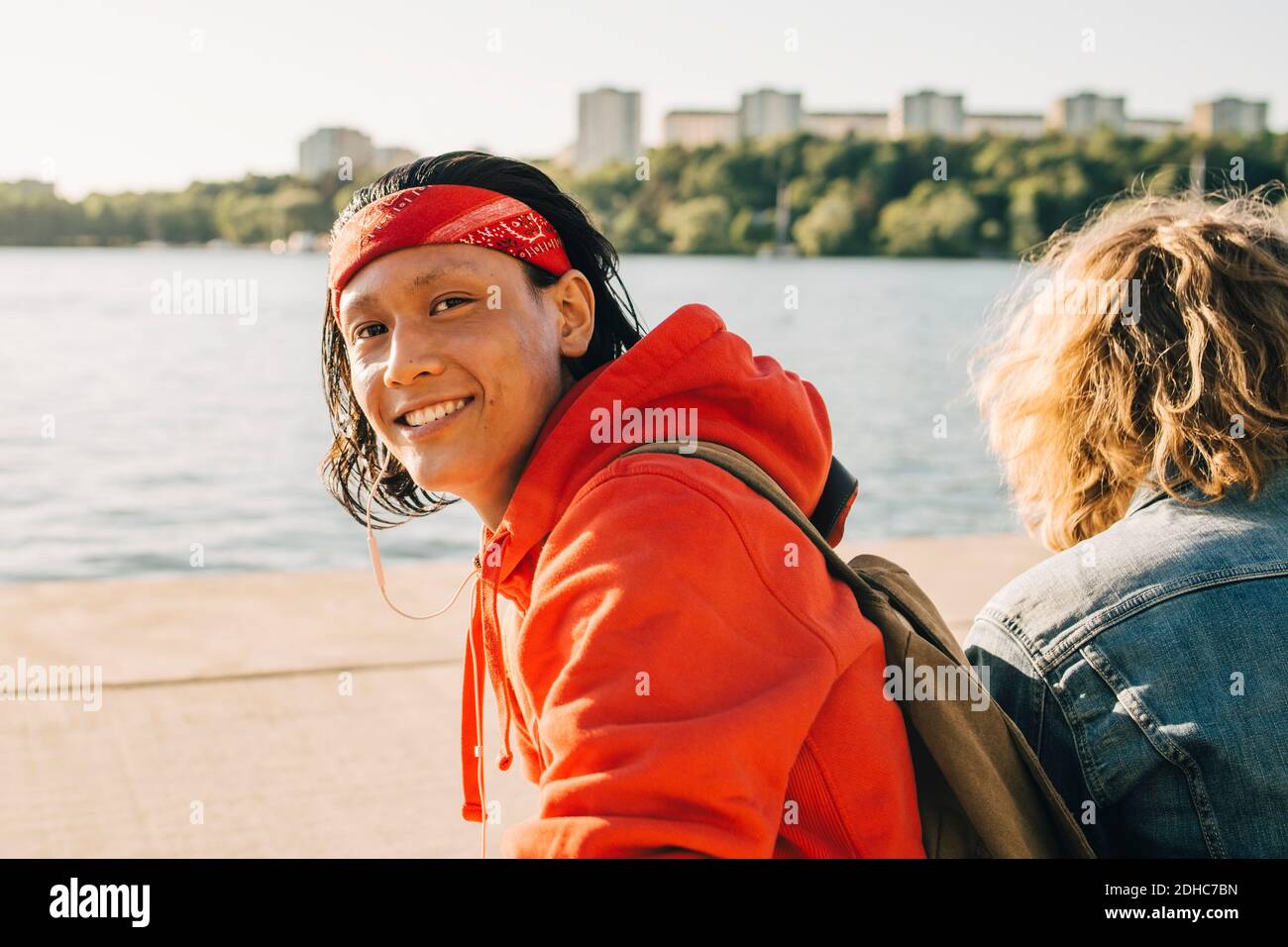 Portrait of smiling young man sitting by friend on promenade during sunny day Stock Photo