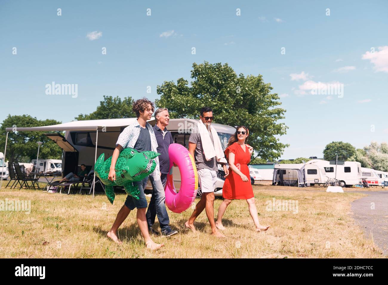 Full length of family with inflatable rings walking on grassy field against sky Stock Photo