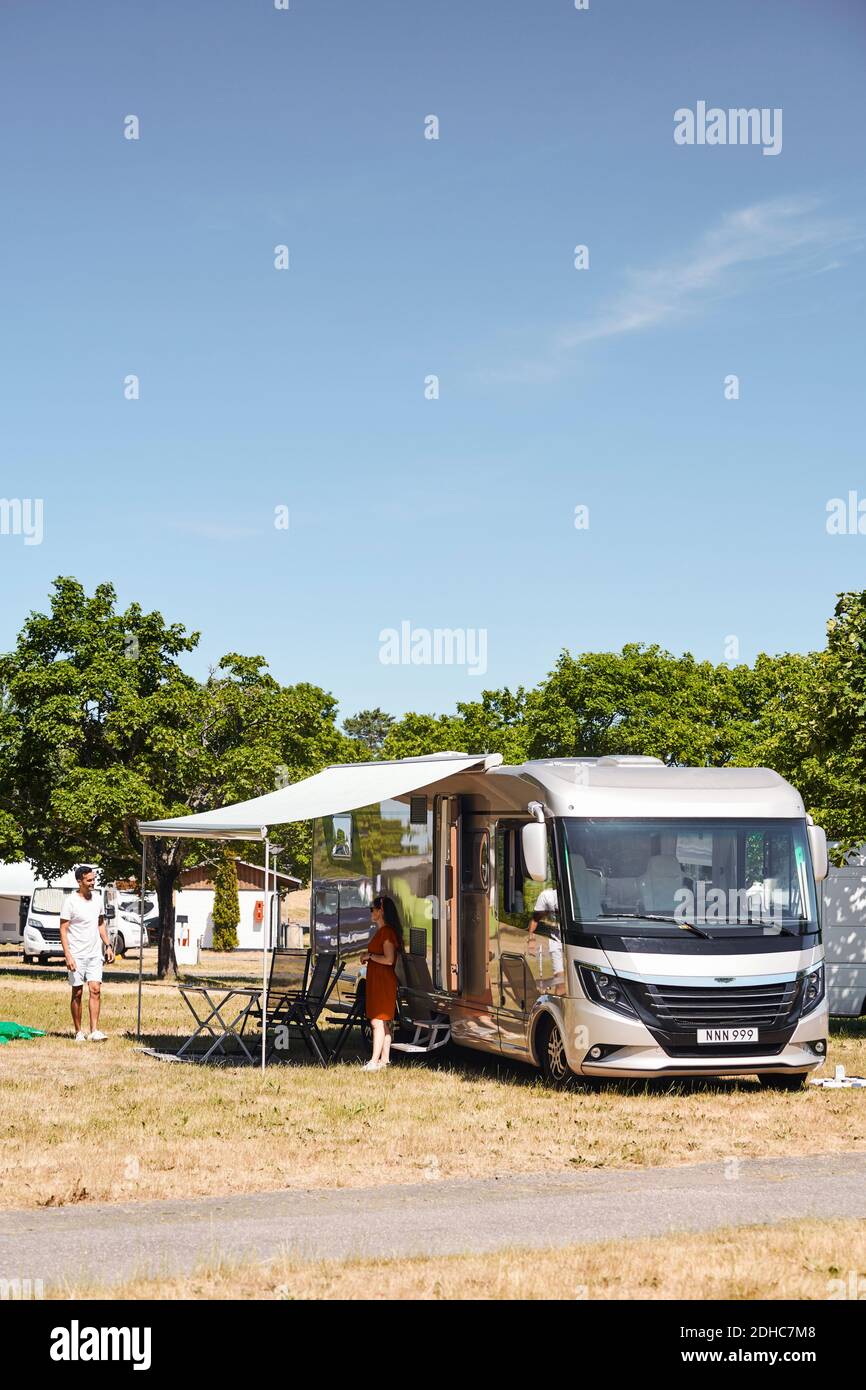 Couple talking while standing outside camper van at trailer park against blue sky Stock Photo