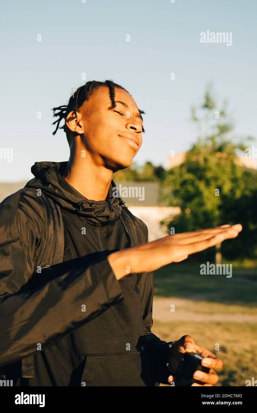 Teenage boy with eyes closed gesturing during sunny day Stock Photo