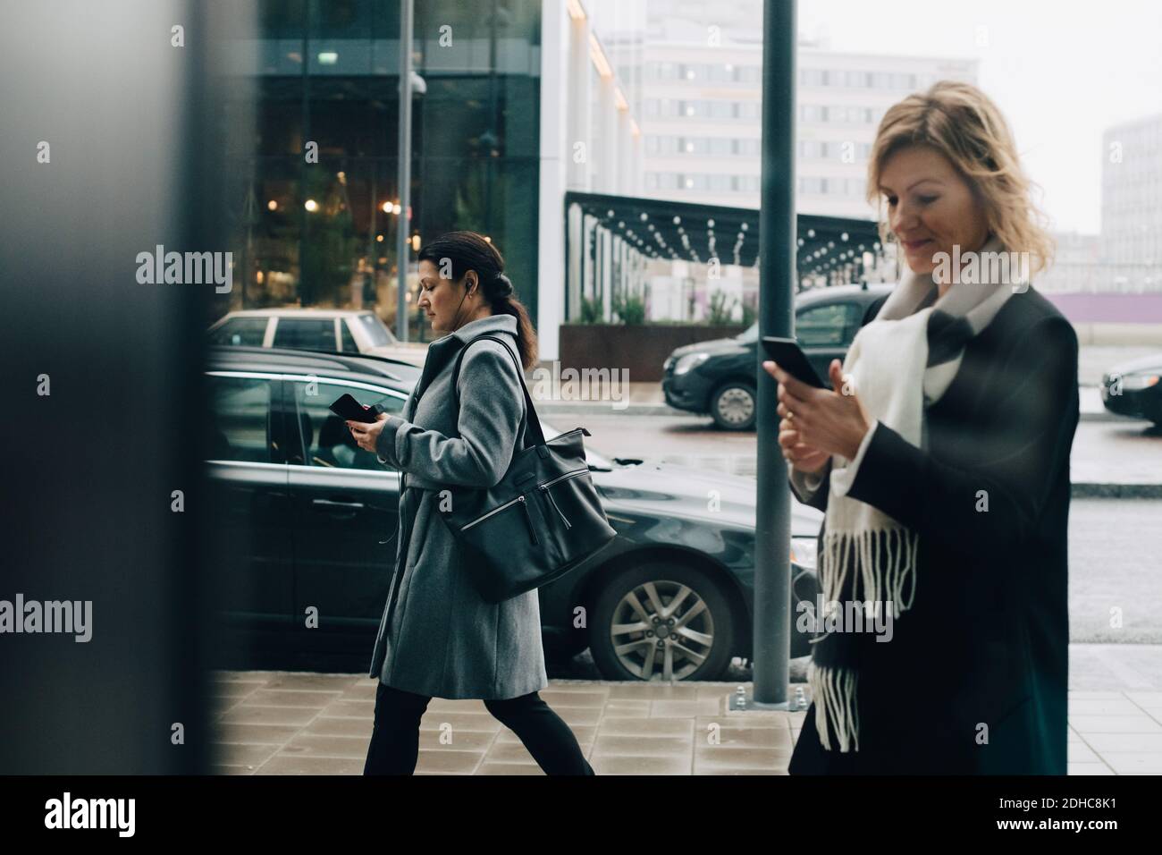 Businesswomen using smart phones while walking on sidewalk in city Stock Photo