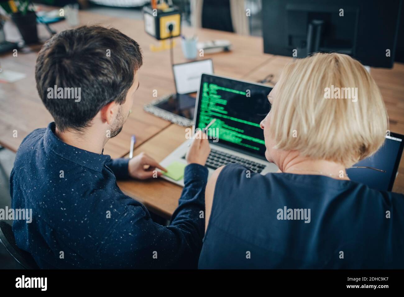 Male and female computer programmers discussing over laptop at desk in creative office Stock Photo