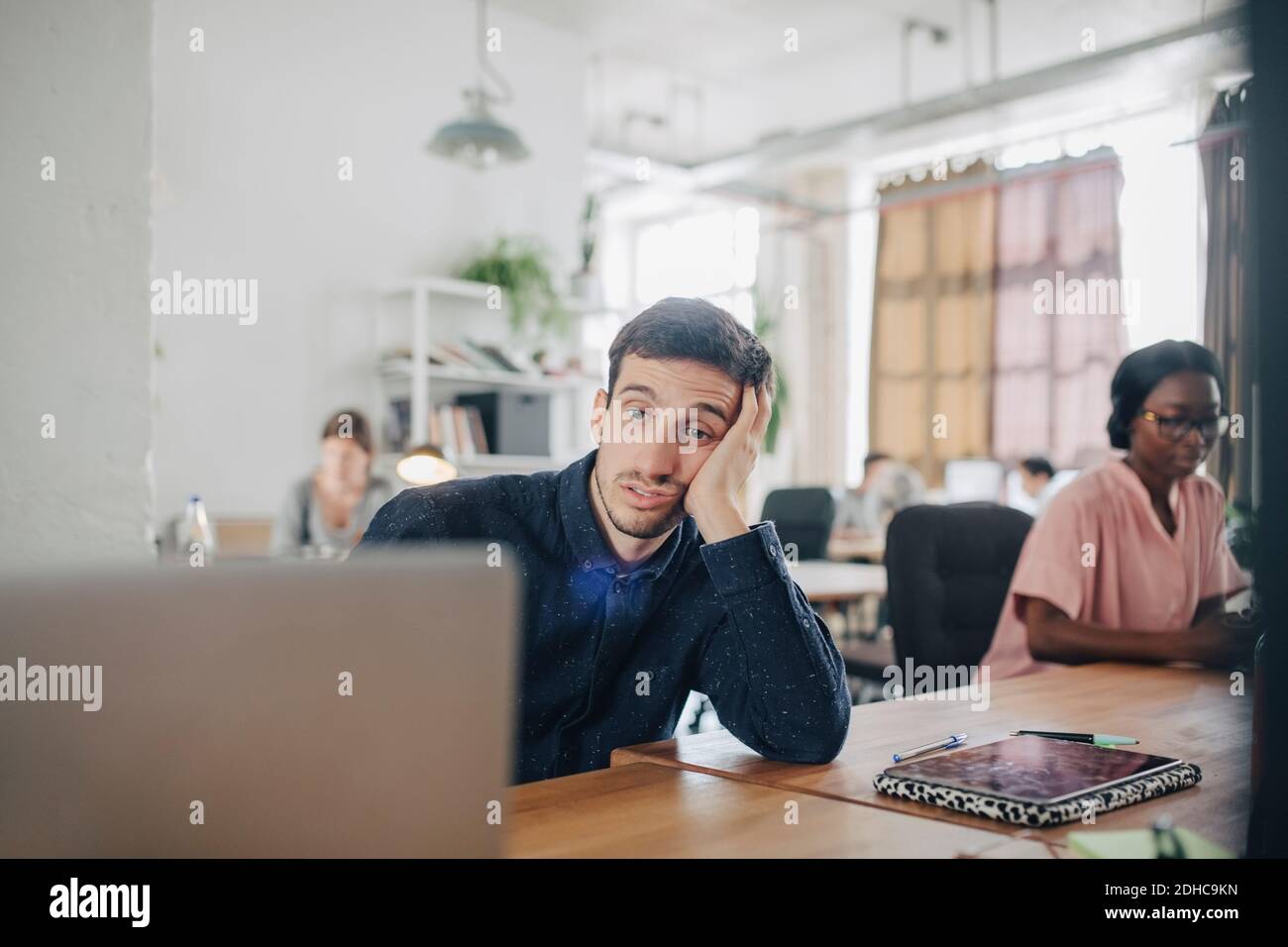 Tired businessman looking at laptop while sitting at desk in creative office Stock Photo