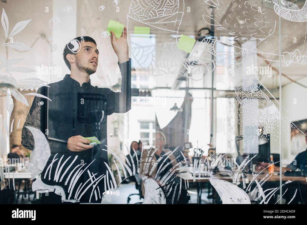 Young creative businessman sticking adhesive note on patterned glass in office Stock Photo