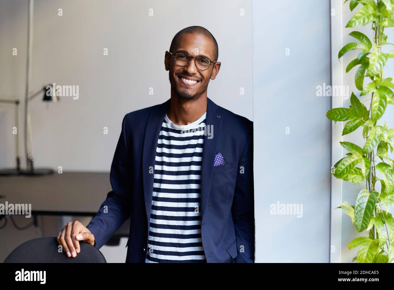 Portrait of smiling male entrepreneur standing by wall in creative office Stock Photo