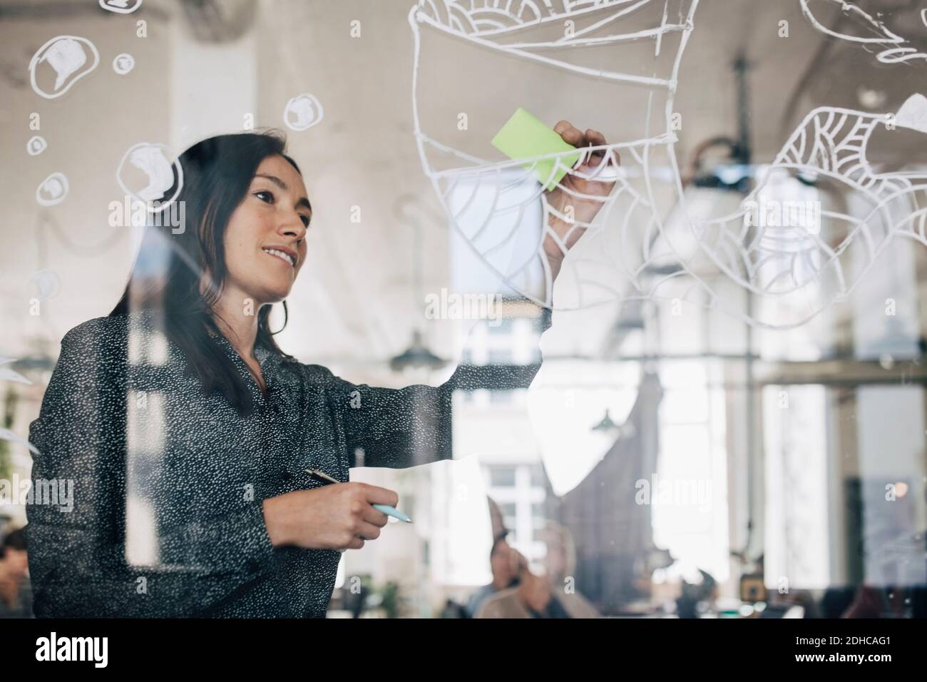Creative businesswoman sticking adhesive note on patterned glass in office Stock Photo