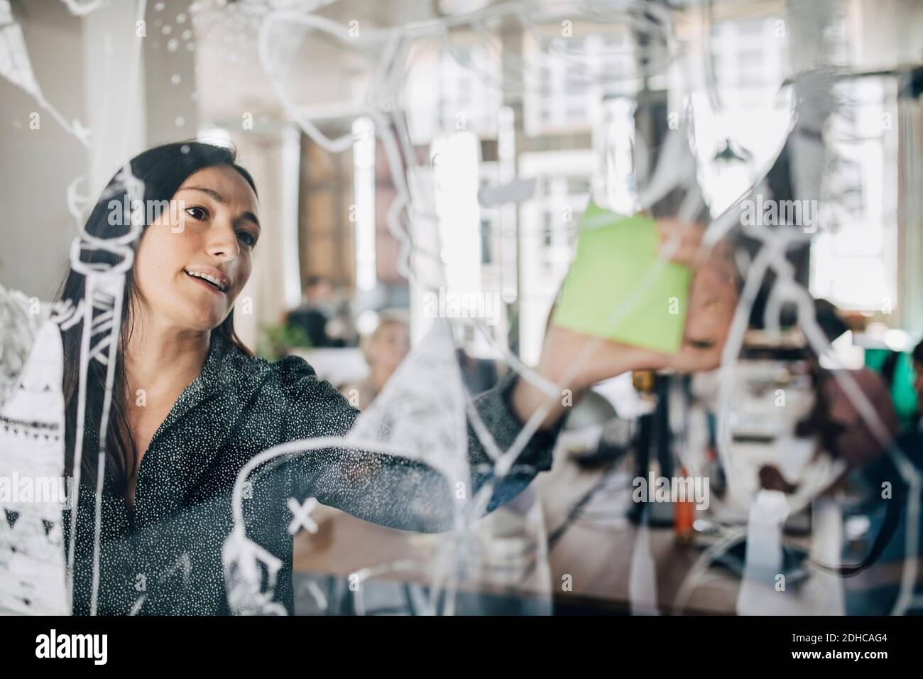 Businesswoman sticking adhesive note on patterned glass in creative office Stock Photo