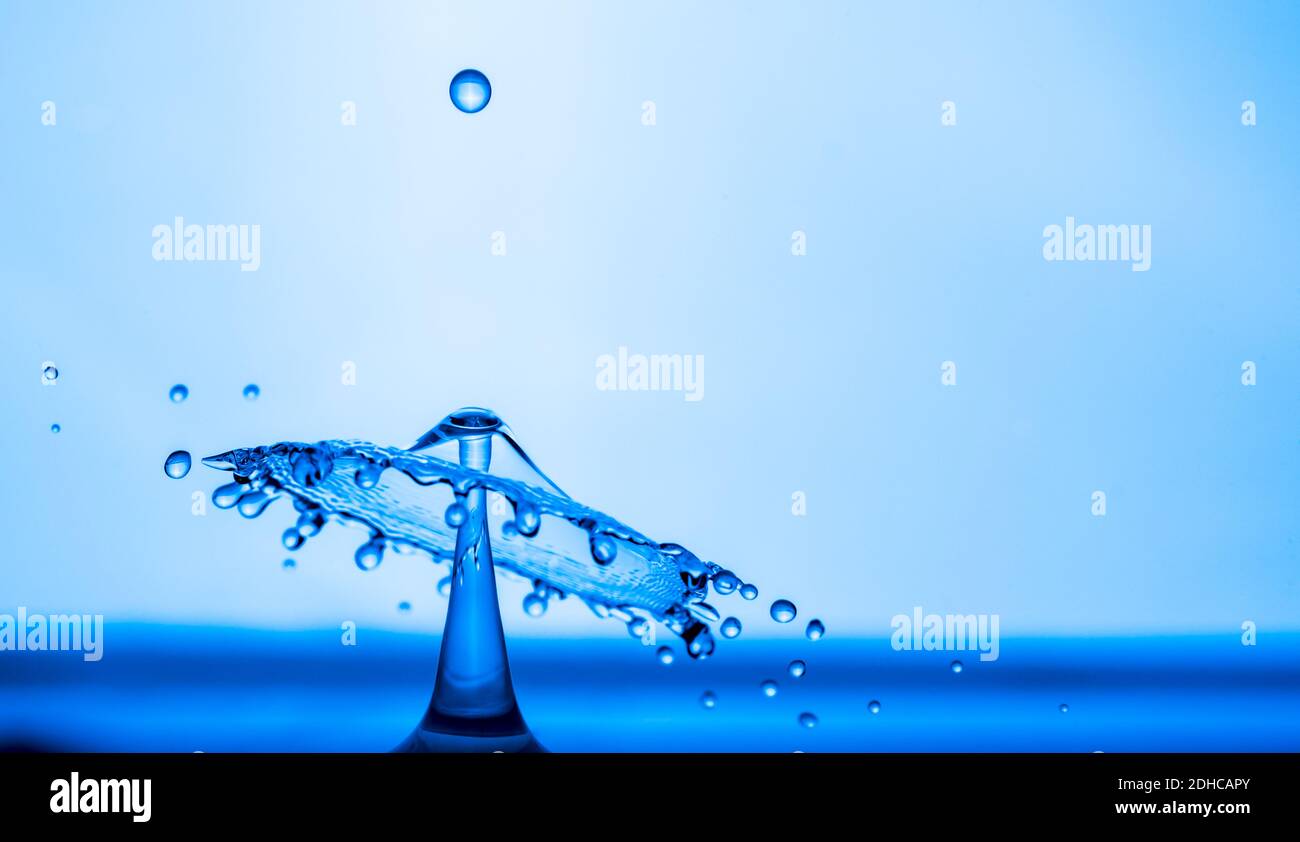 Water drop splashing into blue water surface Stock Photo - Alamy
