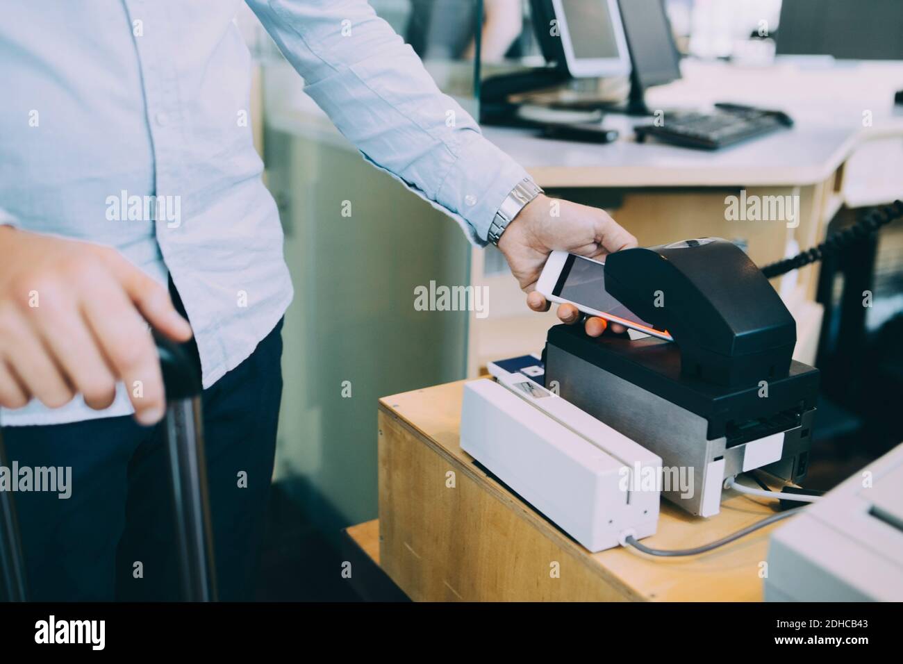 Midsection of businessman scanning ticket on smart phone at airport check-in counter Stock Photo