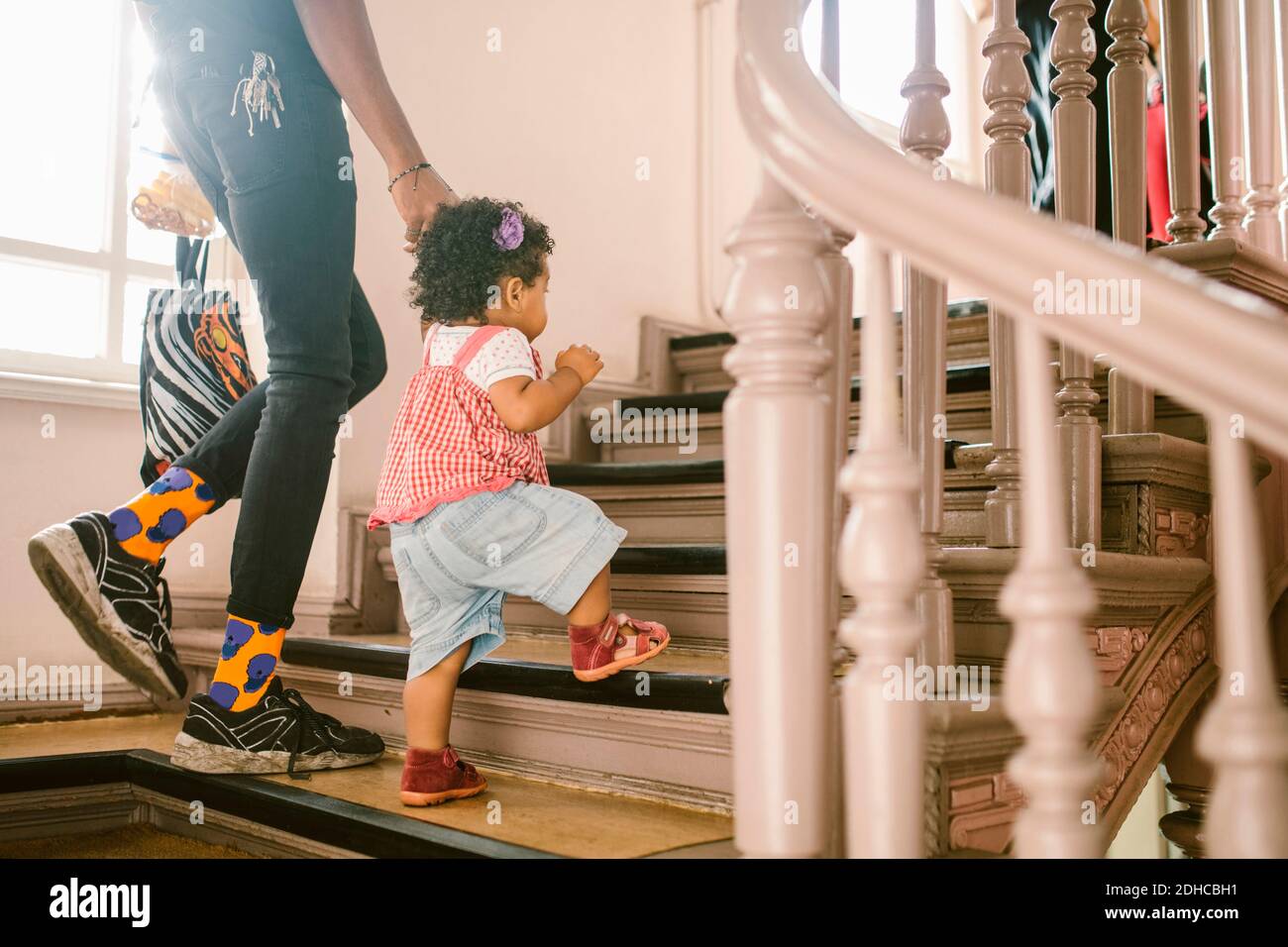 Baby girl holding hand of father while climbing staircase at apartment Stock Photo