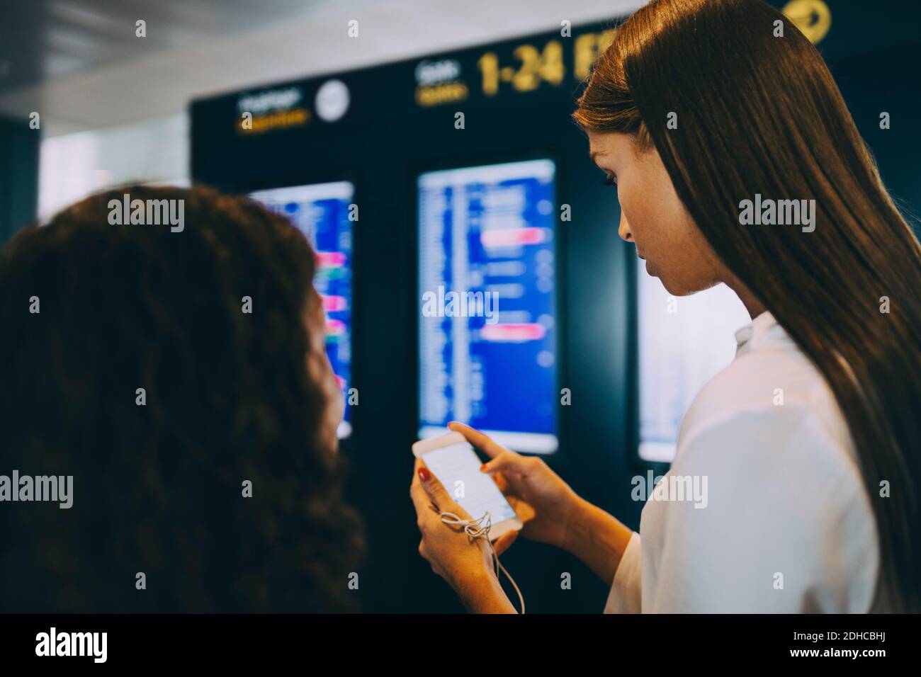 Young businesswoman checking flight timings through smart phone at airport Stock Photo