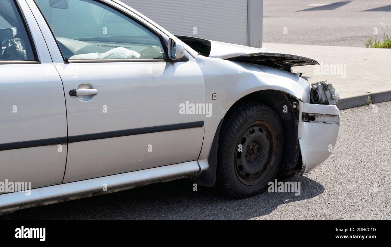 Crashed car standing on road next to curb, side view with demolished front and used airbag inside visible Stock Photo