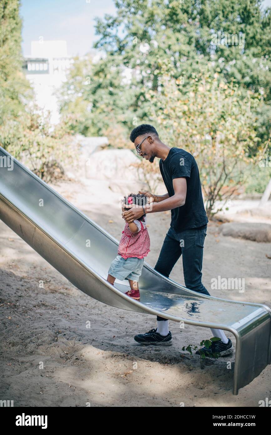 Young man holding hands of daughter walking on slide at playground Stock Photo