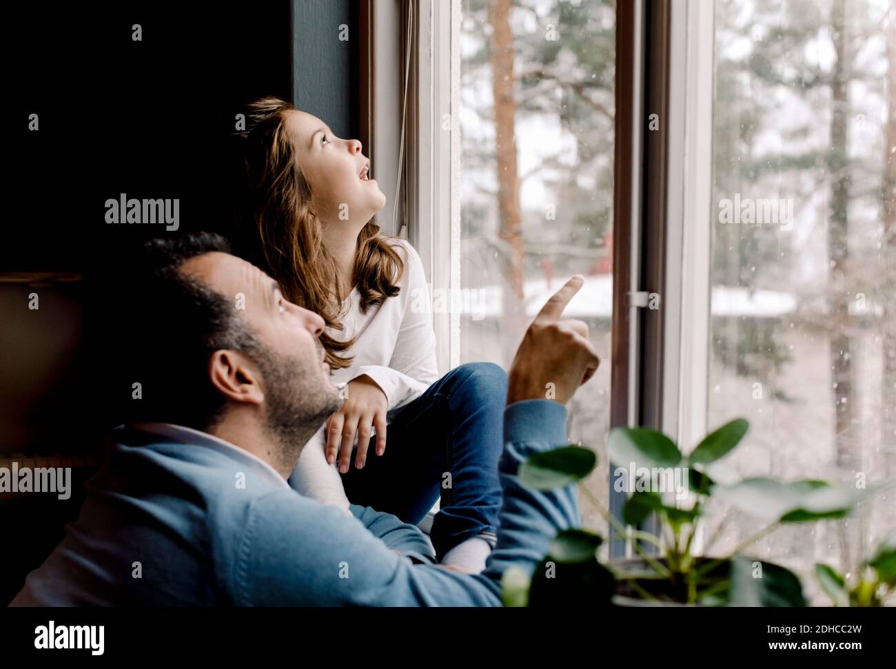 Father and curious daughter looking through window at home Stock Photo
