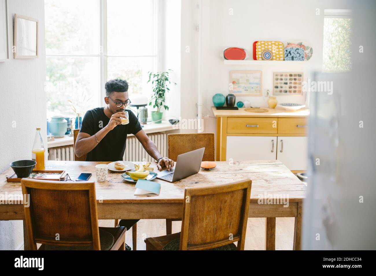 Young man drinking juice while using laptop at table in house Stock Photo