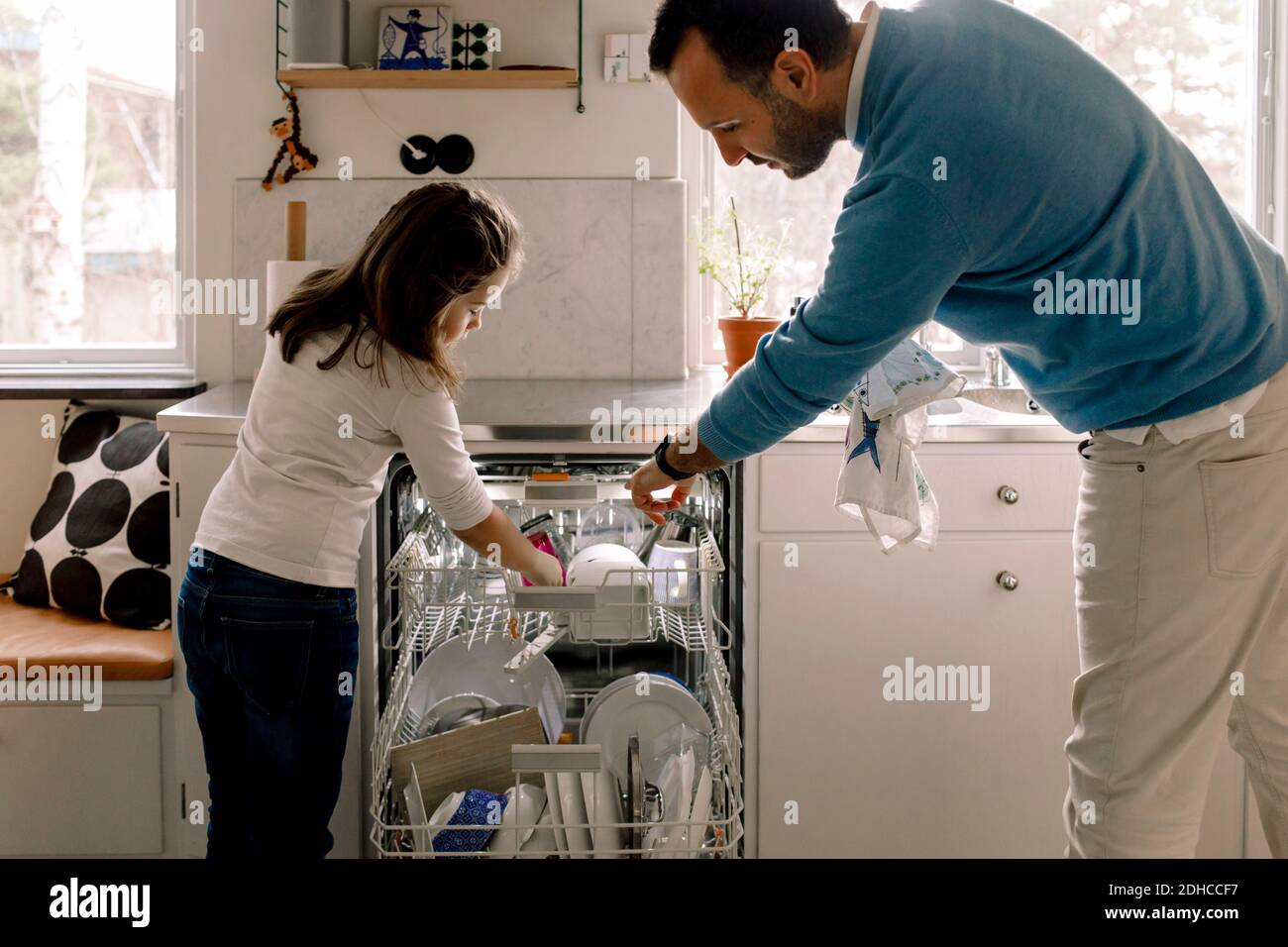 Father and daughter arranging utensils in dishwasher at kitchen Stock Photo