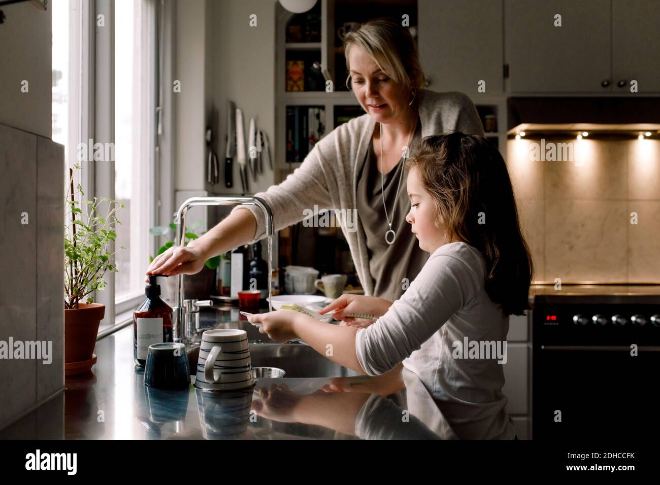https://c8.alamy.com/comp/2DHCCFK/daughter-washing-dishes-while-standing-by-mother-in-kitchen-at-home-2DHCCFK.jpg