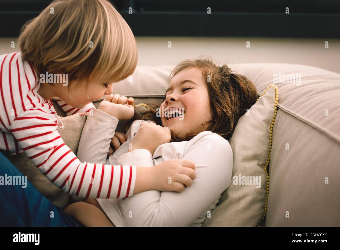 Playful girl tickling cheerful sister on couch at home Stock Photo