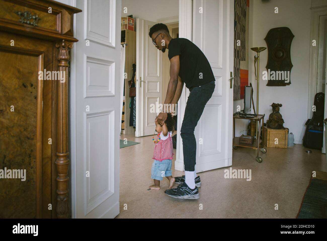 Side view of father assisting daughter in walking at home Stock Photo
