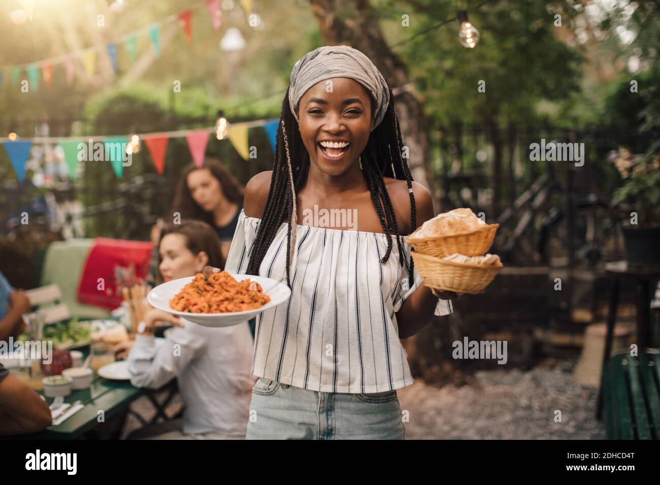 Portrait of smiling young woman carrying food while standing in backyard during garden party Stock Photo