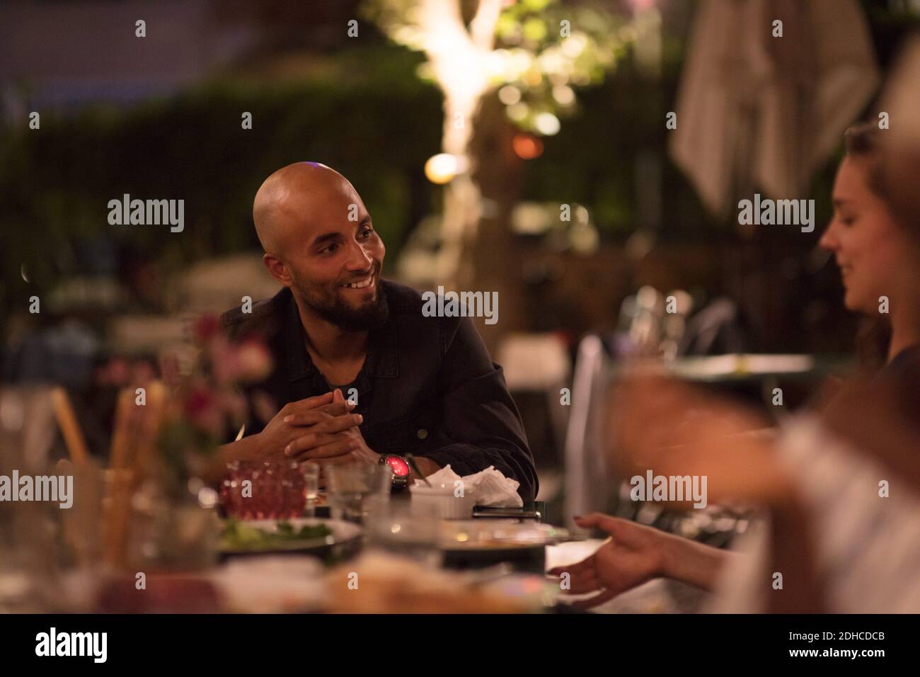 Smiling young man with shaved head looking at female friend while sitting at table during dinner party Stock Photo