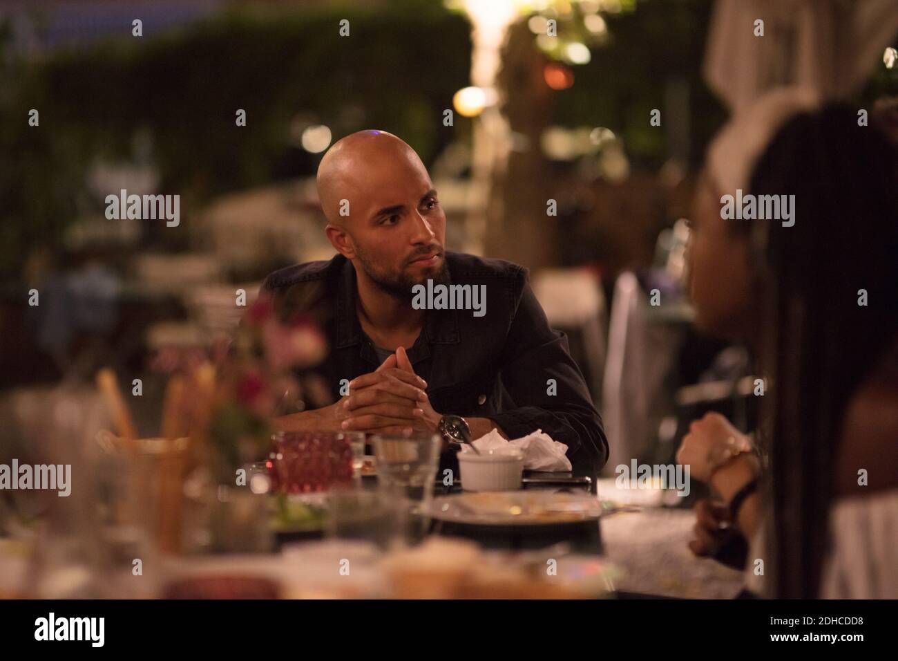 Young man with shaved head looking at female friend while sitting at table during dinner party Stock Photo