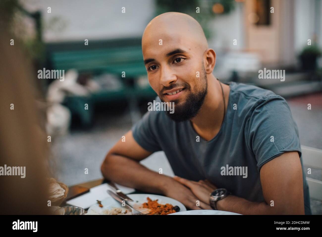 Smiling young man with shaved head looking at female friend during dinner party in backyard Stock Photo