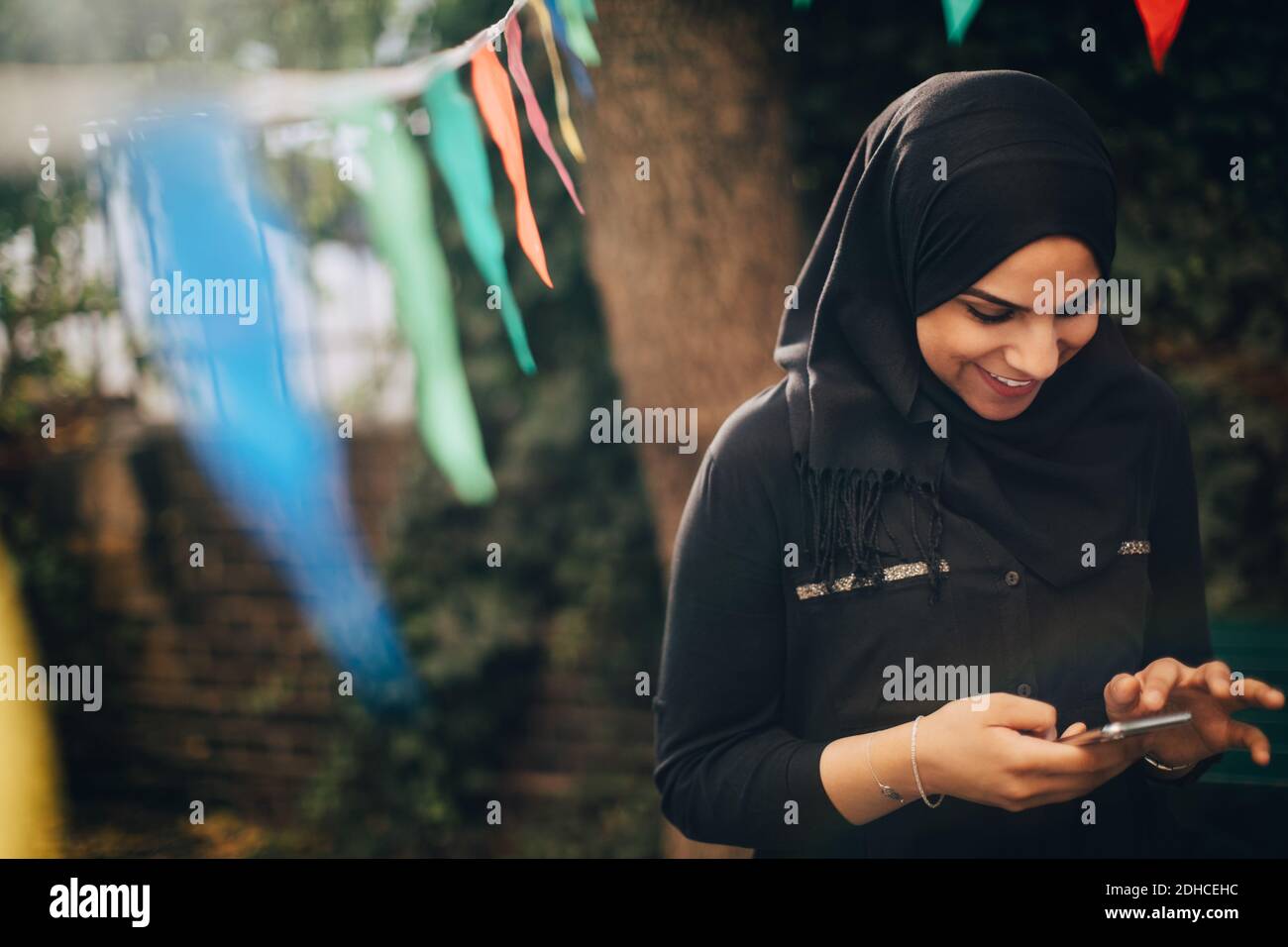 Smiling young woman in hijab using mobile phone at backyard Stock Photo ...